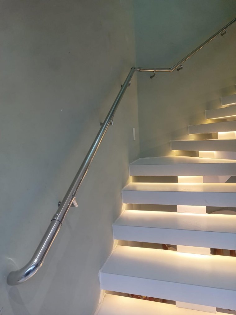 Corrimão de parede em aço inox polido acompanhando uma escada iluminada