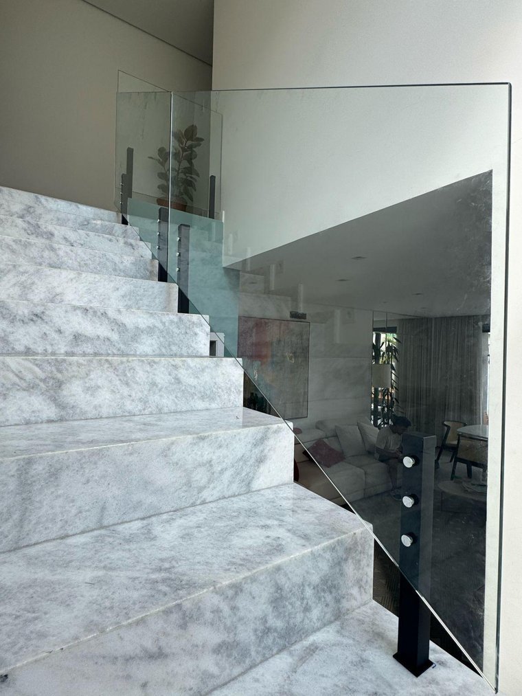 Guarda-corpo de vidro fixado com torres em inox junto a uma escada de pedra clara